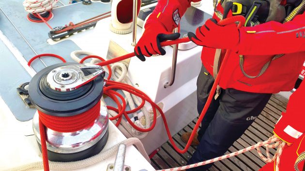 Someone working rope through a winch. The person has gloved hands.